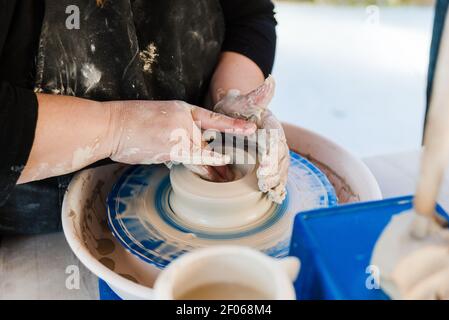 Crop anonyme weibliche Handwerker in Schürze Modellierung Ton Topf auf Wurfrad Stockfoto