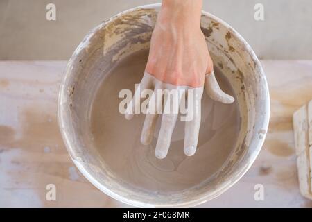 Von oben Ernte anonyme Handwerker neben Tisch stehen und schmutzige Hand aus Eimer mit Ton im Studio bei Tageslicht gefüllt ziehen Stockfoto