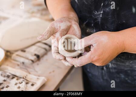 Hoher Winkel der Ernte anonymen Master in schwarz schmutzige Schürze In der Werkstatt stehen und ein Stück Ton in den Händen Formen Neben Tisch mit Werkzeugen für Handwerk Stockfoto