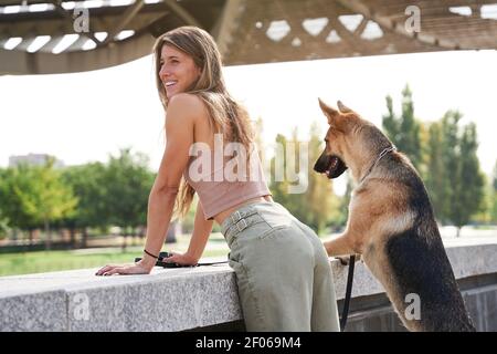 Seitenansicht der fröhlichen weiblichen Besitzer lehnte sich mit Schäferhund Hund an der Grenze am Damm Stockfoto