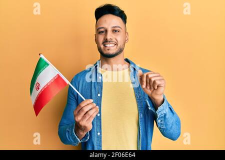 Junger arabischer Mann hält die iranische Flagge lächelnd mit einer Idee oder Frage, die den Finger mit einem glücklichen Gesicht zeigt, Nummer eins Stockfoto