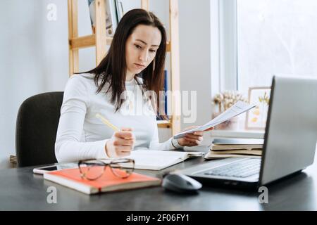 Kleinunternehmen, Selbständigkeit, Kleinstunternehmer, Buchhalter, Eigentumskonzept. Junge Geschäftsfrau arbeitet mit Laptop und Dokument aus dem Büro Stockfoto