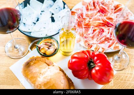 Typisch katalanische oder spanische Küche. Brot mit Tomate, iberischer Schinken, Glas Rotwein, Ziegenkäse, Öl und Knoblauch. Draufsicht auf Lebensmittel zum Abendessen Stockfoto