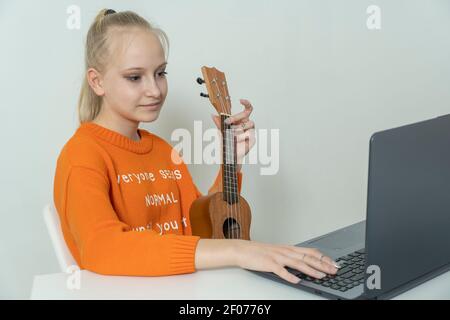 Teenager-Mädchen lernt, die Ukulele zu spielen und schaut in Ihr Laptop Stockfoto