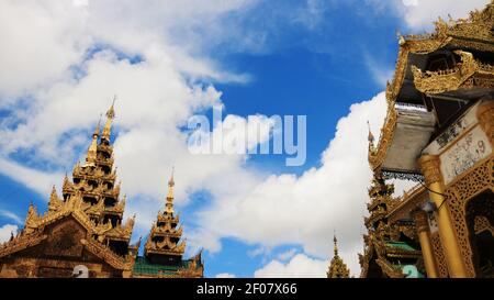 Fassaden von zwei Tempeln mit goldenem und verschlungenem Design und einem wolkigen und blauen Himmel im Shwedagon Pagoda Complex, Yangon, Myanmar aufgenommen Stockfoto