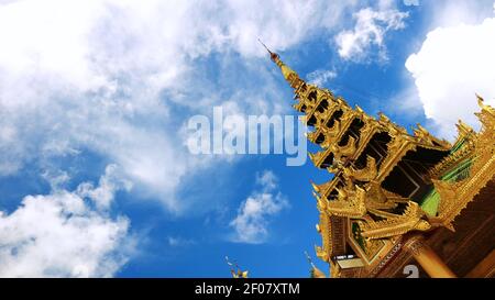 Gekippte Aufnahme eines goldenen Dachs eines kleinen Tempels und eines wolkigen und blauen Himmels im Shwedagon Pagoda Complex, Yangon, Myanmar (Burma) Stockfoto