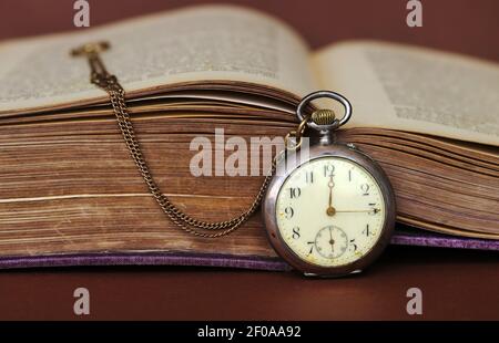 Eine antike Taschenuhr lehnt sich an ein altes Buch mit Vergilbte Seiten Stockfoto