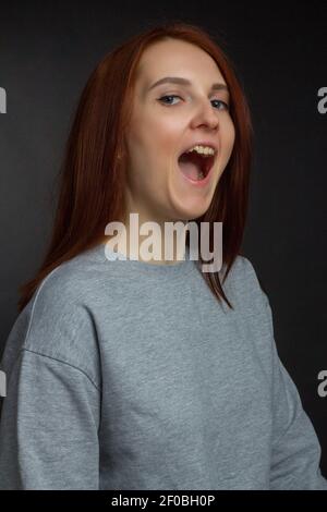 Rothaarige junge Mädchen auf schwarzem Hintergrund in einem grauen T-Shirt Stockfoto