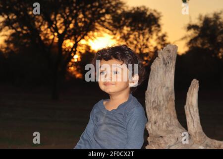 Ein indisches schönes lächelndes kleines Knabenkind, das im Feld draußen am Sonnenuntergang sitzt, indien. Konzept für lächelnde Kinder, Stolz des Landes heute childr Stockfoto