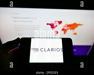 Person, die Mobiltelefon mit Logo des US-Batterieherstellers Clarios auf dem Bildschirm vor der Website des Unternehmens mit Karte hält. Konzentrieren Sie sich auf die Telefonanzeige. Stockfoto