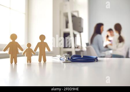 Stethoskop und kleine hölzerne Familienfiguren auf dem Arzttisch Im Krankenhaus Stockfoto