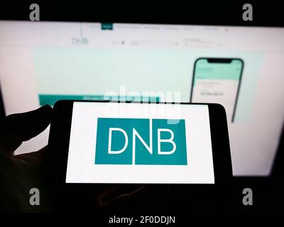 Person, die ein Mobiltelefon mit dem Logo des norwegischen Finanzdienstleisters DNB ASA auf dem Bildschirm vor der Unternehmenswebsite hält. Konzentrieren Sie sich auf die Telefonanzeige. Stockfoto