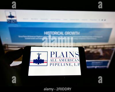 Person, die Mobiltelefon mit Logo der amerikanischen Pipeline-Firma Plains All American Pipeline auf dem Bildschirm vor der Webseite hält. Konzentrieren Sie sich auf die Telefonanzeige. Stockfoto