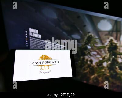 Person, die Smartphone mit dem Logo des kanadischen Cannabisunternehmens Canopy Growth Corporation auf dem Bildschirm vor der Website hält. Konzentrieren Sie sich auf die Telefonanzeige. Stockfoto