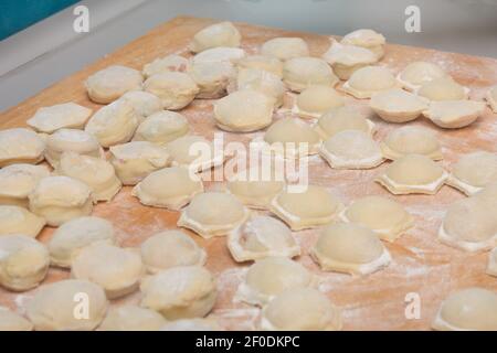 Viele hausgemachte Knödel auf dem Tisch mit Mehl. Rohe Ravioli sind bereit zum Kochen. Nahaufnahme, selektiver Fokus. Stockfoto