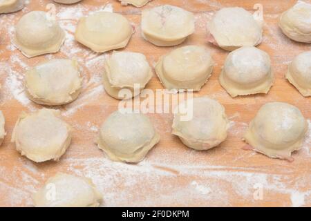 Hausgemachte Knödel mit Fleisch auf Holztisch mit Mehl. Ravioli zum Kochen Abendessen. Nahaufnahme, selektiver Fokus. Stockfoto