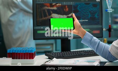 Nahaufnahme der Wissenschaftlerin Frau hält Smartphone mit grünem Mockup in modern ausgestatteten Labor. Team von Mikrobiologen tun Impfstoffforschung Schreiben auf Gerät mit Chroma-Taste, isolierte Anzeige. Stockfoto