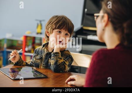 Netter Junge im Gespräch mit Mama, während mit digitalen Tablet. Sohn, der zu Hause mit seiner Mutter spricht. Stockfoto