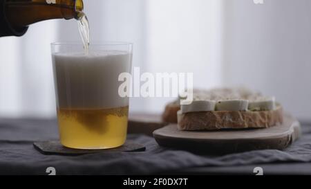 Weizenbier in einem Glas neben Ciabatta-Sandwiches mit Mozzarella und Pesto auf Leinentuch gießen, breites Foto Stockfoto