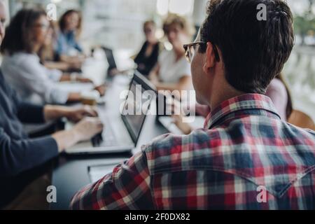 Über ihrer Schulter Blick auf Mann im Büro Sitzung sitzen. Mann in Gelegenheitskleidung, der an einem Treffen mit Kollegen teilnimmt, die in der Nähe des Konferenztisches sitzen Stockfoto