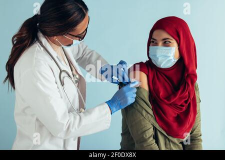 Muslimische Frau trägt Gesichtsmaske bekommen covid-19 Impfstoff von einer Ärztin erschossen. Gesundheitsexperte, der nach dem gi ein Pfand auf den Arm einer Frau legt Stockfoto