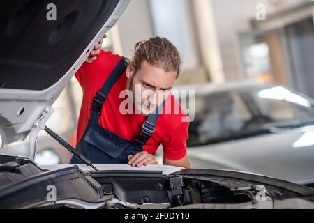 Reparaturman untersucht die Innenseiten einer offenen Haube Stockfoto