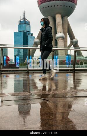 Eine junge Frau auf dem Skywalk vor dem Oriental Pearl Tower in Shanghais Lujiazui, Bezirk Pudong, China an einem kalten regnerischen frühen Frühlingstag. Stockfoto