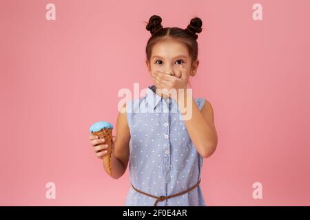 Kleines Mädchen hält Eis in Waffelkegel auf rosa Hintergrund. Kind mit Halsschmerzen berühren ihren Hals. Halsschmerzen krank Stockfoto