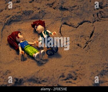 Zwei Spielzeugfiguren liegen auf kinetischem Sand, neben einer Zeichnung eines Herzens mit einem Pfeil durch ihn. Stockfoto