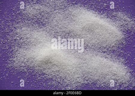 Granulierte weiße Zuckerstruktur und Hintergrund auf violettfarbenem Papier Blatt Stockfoto