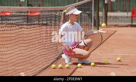 Mädchen Tennisspielerin sitzt auf dem Platz und wirft Bälle. Stockfoto