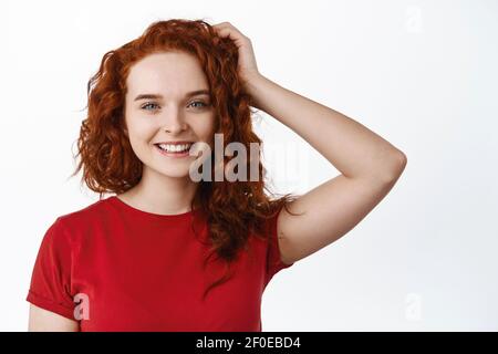 Nahaufnahme Porträt von schönen Rothaarfrauenmodell mit lockigen Frisur, berühren Kopf und lächelnde weiße Zähne, immer neue Frisur getan, stehen Stockfoto