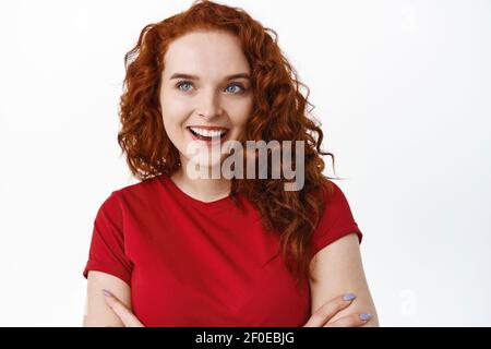 Close-up von dummen schönen Mädchen mit Ingwer lockiges Haar, Blick auf die linke Seite Logo oder Werbung, lächelnd zufrieden und entschlossen zu kaufen Stockfoto