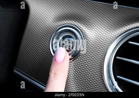 Autofahrer, der den Motor mit dem Start-Stopp-Motor-Knopf angelassen hat. Drücken Sie die Motor-Start- und -Stopp-Taste mit dem Finger. Moderne Innenausstattung. Handfinger Pre Stockfoto