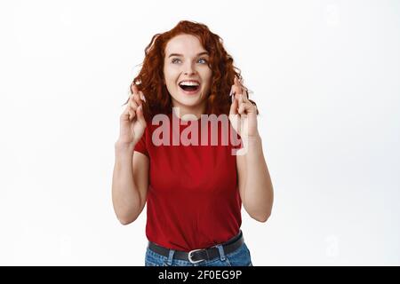 Aufgeregt junge rothaarige Mädchen Kreuz Finger für viel Glück und lächelnd amüsiert, starrte auf obere linke Ecke Werbung, wollen zu kaufen oder haben Stockfoto