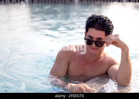 Porträt eines attraktiven jungen Mannes in Sonnenbrille auf Kante ruhen Des Swimmingpools Stockfoto