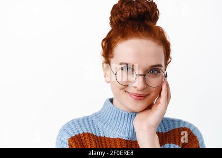 Nahaufnahme Porträt der schönen jungen Studentin mit Ingwer Haar gekämmt in Bun, Brille tragen, erröten niedlich, lächelnd und berührendes Gesicht Stockfoto