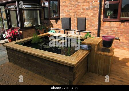 Pflanzen im Garten und Fischteich auf der Terrasse Wasserpflanzen Blumen Holztopf Pflanzen Frühlingsblumen Gartensockel Ziegelgebäude Pflanzen elegant draußen Stockfoto