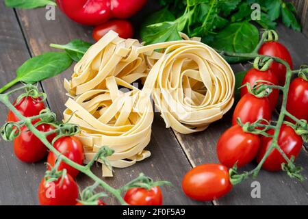 Bunte rohe Pasta Tagliatelle Zutaten auf Holztisch.Nahaufnahme Pasta frische Kirschtomaten, Spinat und Petersilie.Gemüse und gesunde Ernährung Stockfoto