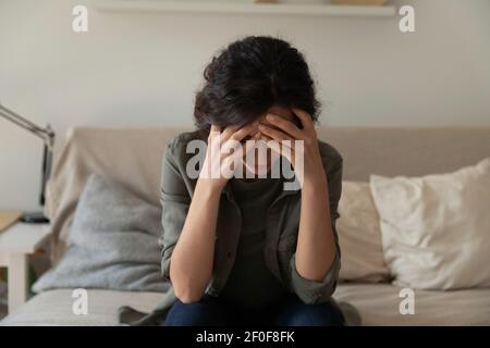 Frustriert depressive tausendjährige Frau sitzen auf der Couch allein umarmen Kopf Stockfoto