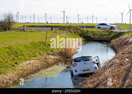 Rye, East Sussex, Großbritannien. März 2021, 7th. Der weiße Hyundai i10 stürzte durch eine hölzerne Einzäunungsmauer und landet halb in einem Wassergraben, der parallel zur Hauptstraße A259 zwischen Rye, East Sussex und Ashford, Kent verläuft. Foto-Kredit: Paul Lawrenson /Alamy Live Nachrichten Stockfoto