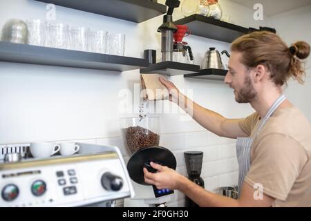 Mann gießt Kaffeebohnen in Kaffeemühle Stockfoto