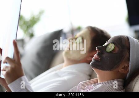 Junger Mann und Frau liegen auf der Couch mit feuchtigkeitsspendenden Gesicht Masken Stockfoto