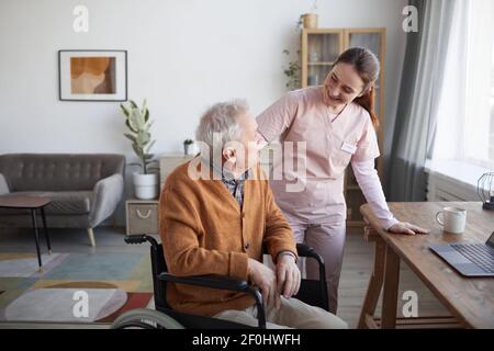 Porträt von lächelnden Krankenschwester hilft älteren Mann im Rollstuhl im Altersheim, kopieren Raum Stockfoto