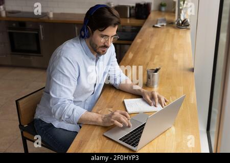 Nahaufnahme fokussierter Mann mit Kopfhörer und Brille auf dem Laptop Stockfoto