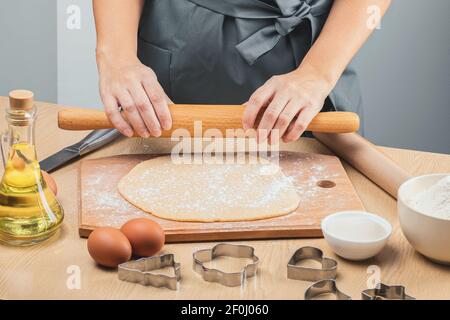 Ein Mädchen in einer grauen Schürze hält einen hölzernen Nudelholz in der Hand und bereitet sich darauf vor, den Teig zum selbstgebackenen Backen, Kekse, auszurollen. Seitenansicht. Stockfoto