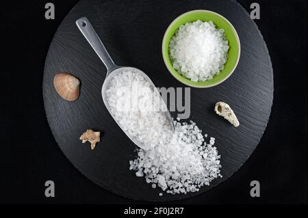 Kleine Porzellanschüssel und Messlöffel voll Meersalz auf Schwarze Schale Stockfoto