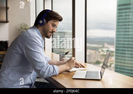 Nahaufnahme fokussierter Mann, der Kopfhörer trägt und sich Notizen macht Stockfoto