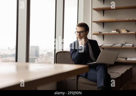 Nachdenklicher ernster Geschäftsmann trägt eine Brille, die das Kinn berührt, und überlegt die Strategie Stockfoto