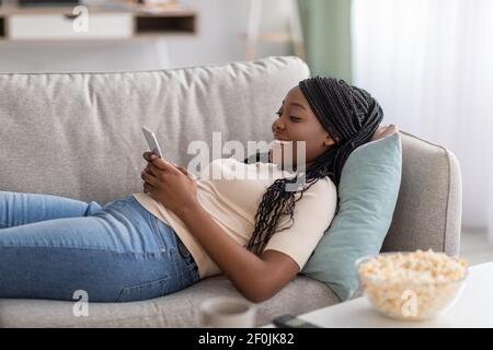 Glückliche schwarze Dame auf der Couch mit Handy liegen Stockfoto
